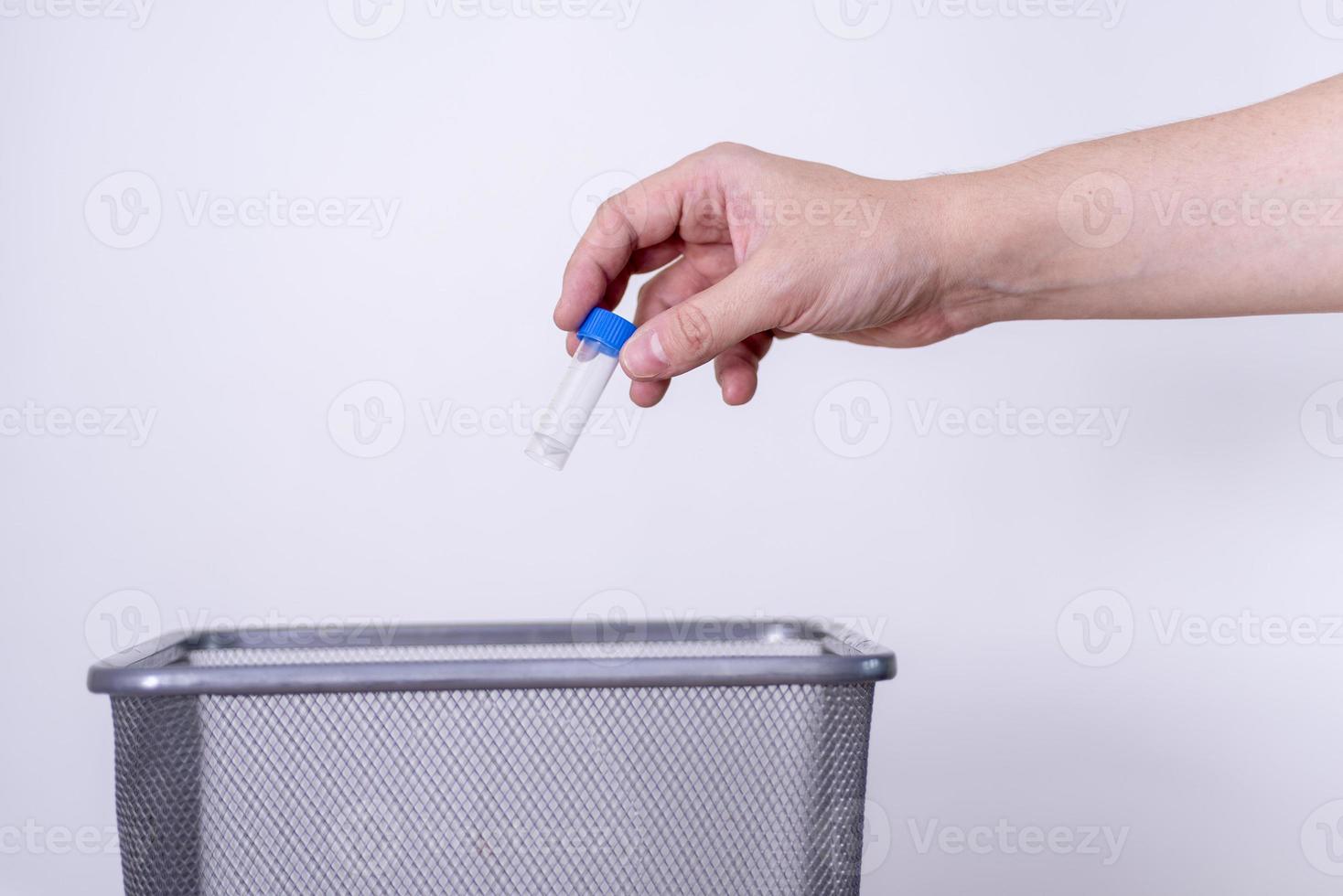 The hand tosses the blue tube into the trash against the gray background. photo