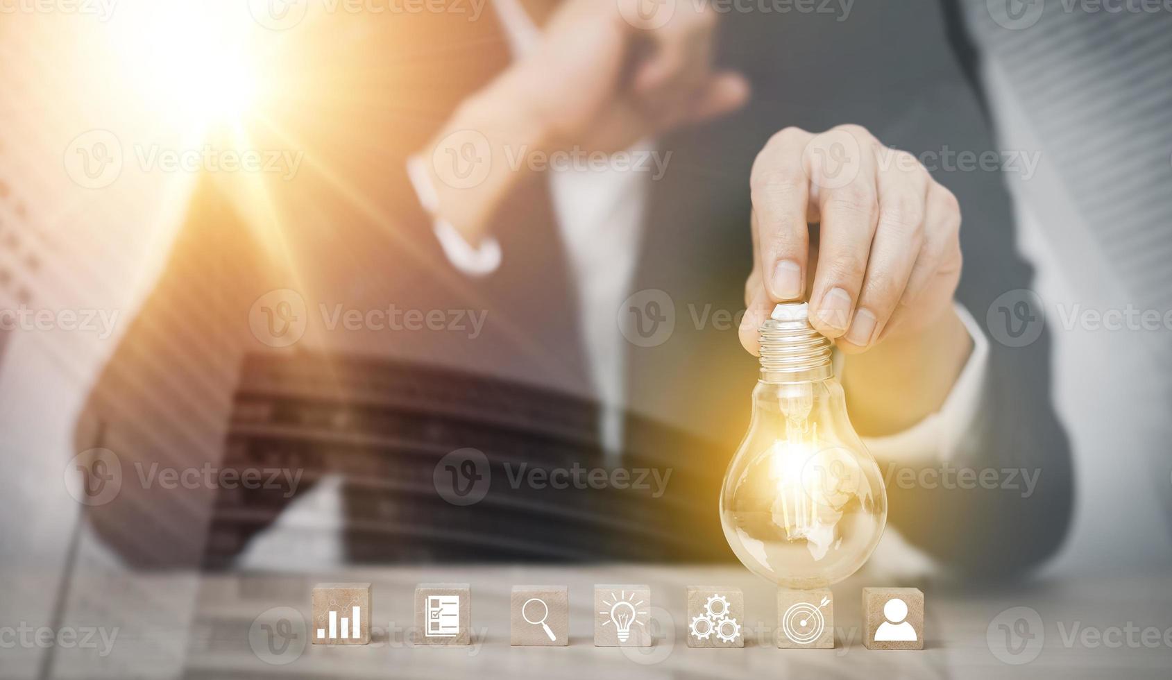 Businessman hand holding light bulb with icon on wood cube and   working on desk, Creativity and innovation are keys to success.Concept of new idea and innovation with Brain and light bulbs, photo