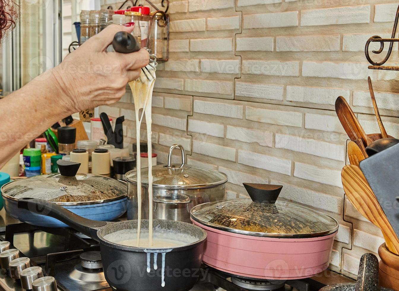 Chef stirs the bechamel sauce, which is cooked on gas stove, into saucepan photo