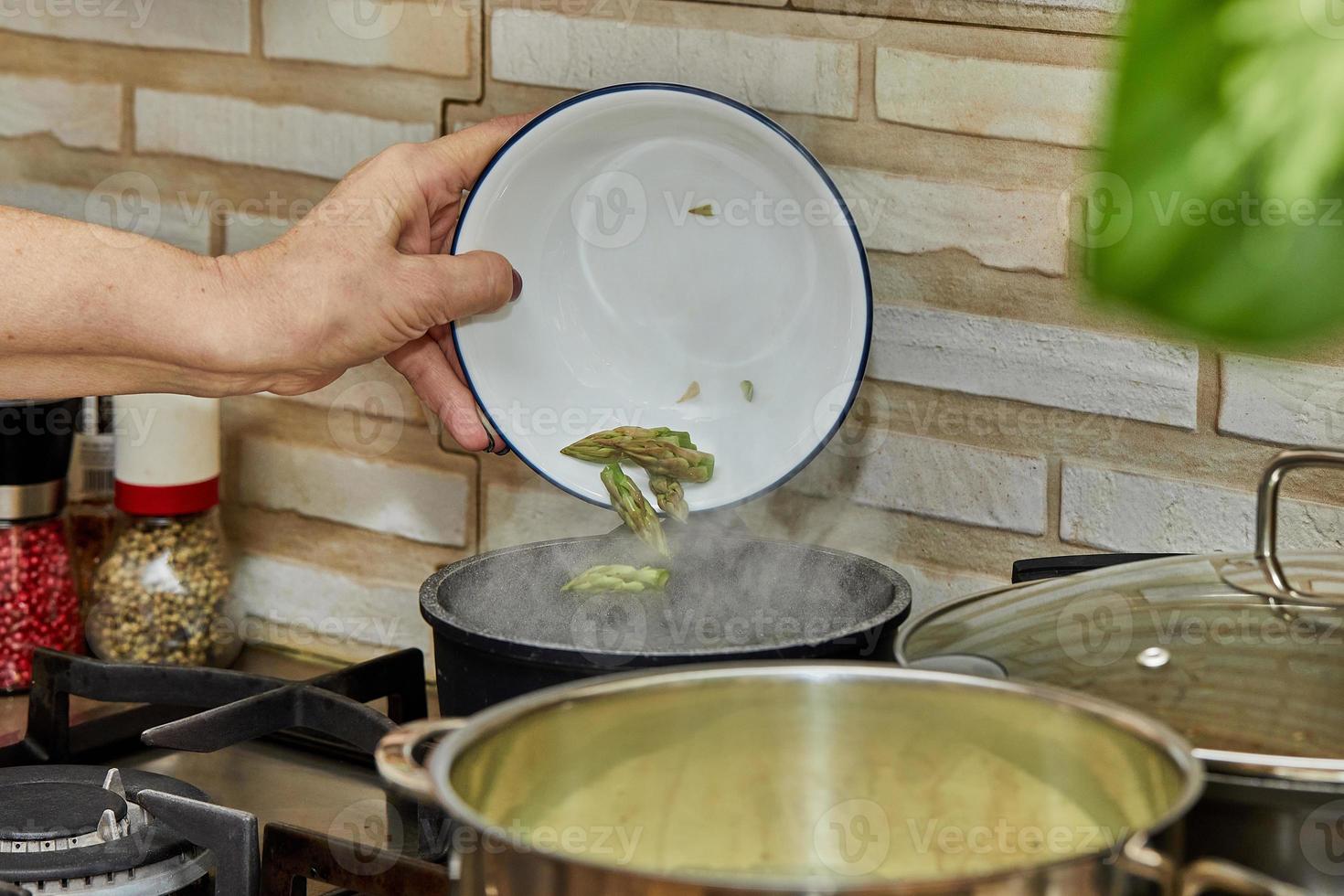 Chef throws asparagus heads into a pot on a gas stove photo