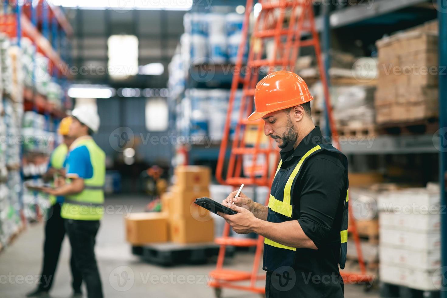 Professional manager man employee using tablet check stock working at warehouse. Worker wearing high visibility clothing and a hard hat, helmet and checking and count up goods or boxes for delivery. photo