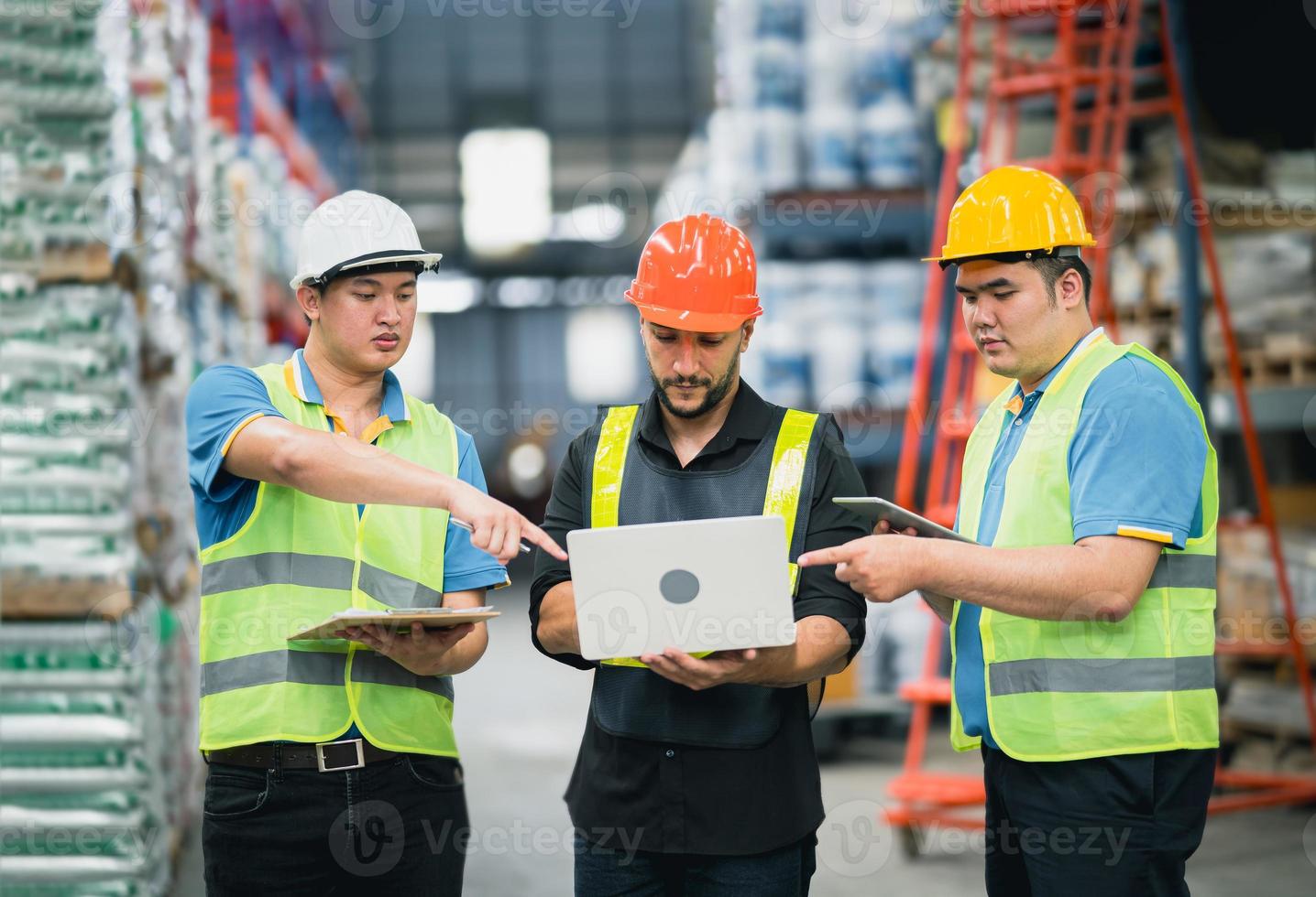 Manager man using laptop check stock and co-worker point finger to laptop at warehouse. Worker wearing high visibility clothing and hard hat, helmet to checking count up goods or boxes for delivery. photo