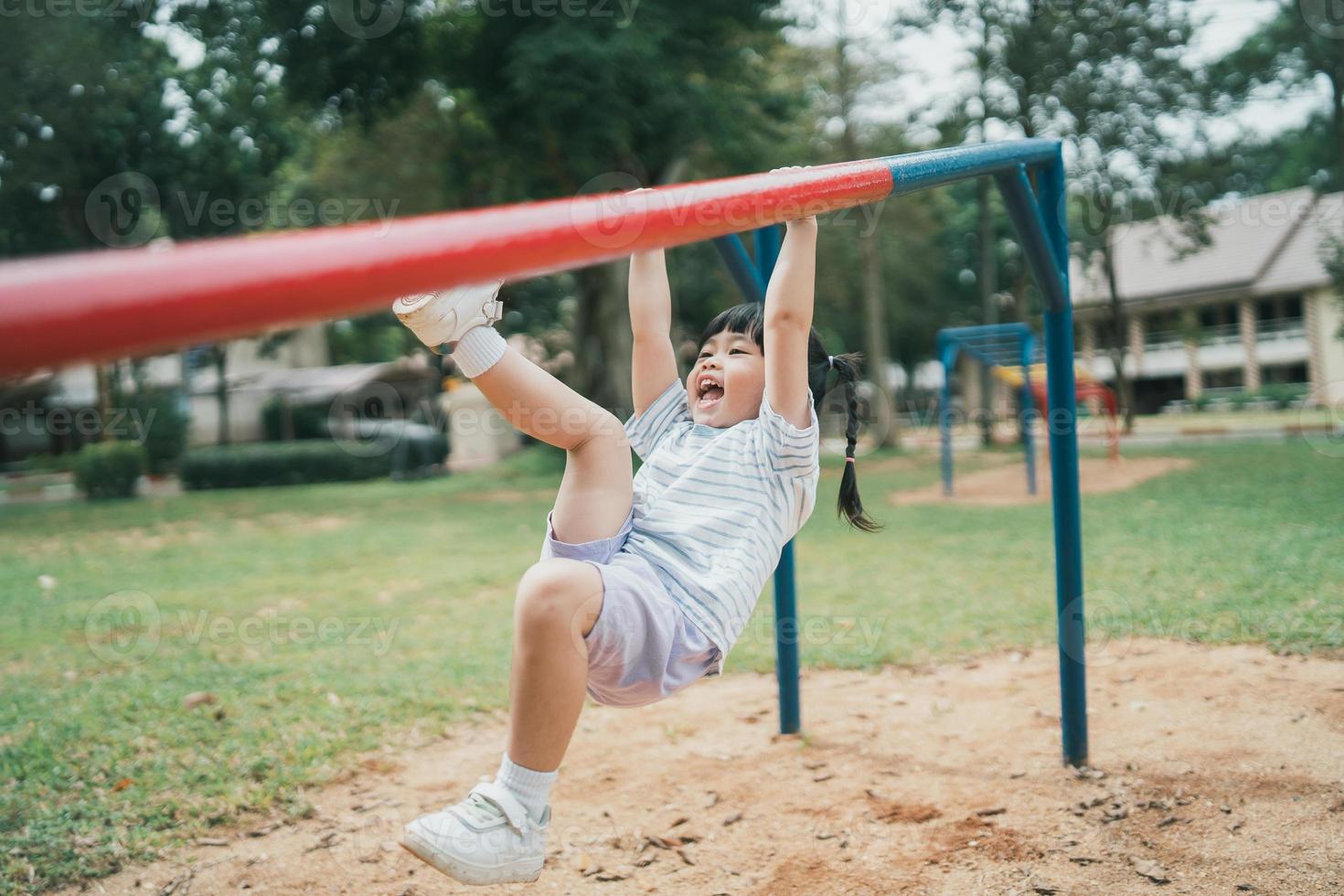 Cute asian girl play on school or kindergarten yard or playground. Healthy summer activity for children. Little asian girl climbing outdoors at playground. Child playing on outdoor playground. photo