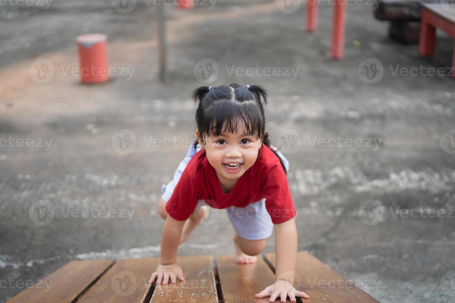 Cute asian girl play on school or kindergarten yard or playground. Healthy summer activity for children. Little asian girl climbing outdoors at playground. Child playing on outdoor playground. photo