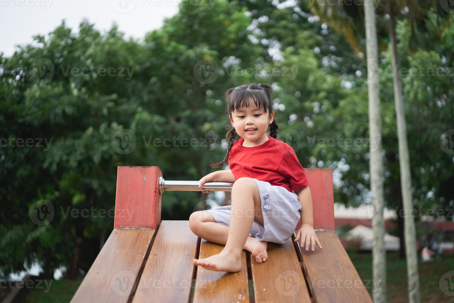 Cute asian girl play on school or kindergarten yard or playground. Healthy summer activity for children. Little asian girl climbing outdoors at playground. Child playing on outdoor playground. photo