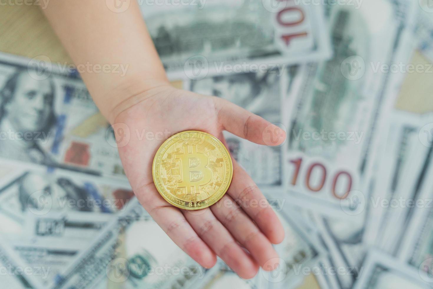 Close up of hand baby holding gold bitcoin crypto currency blockchain on dollar bill background on table. Crypto currency blockchain Saving investment wealth concept. photo