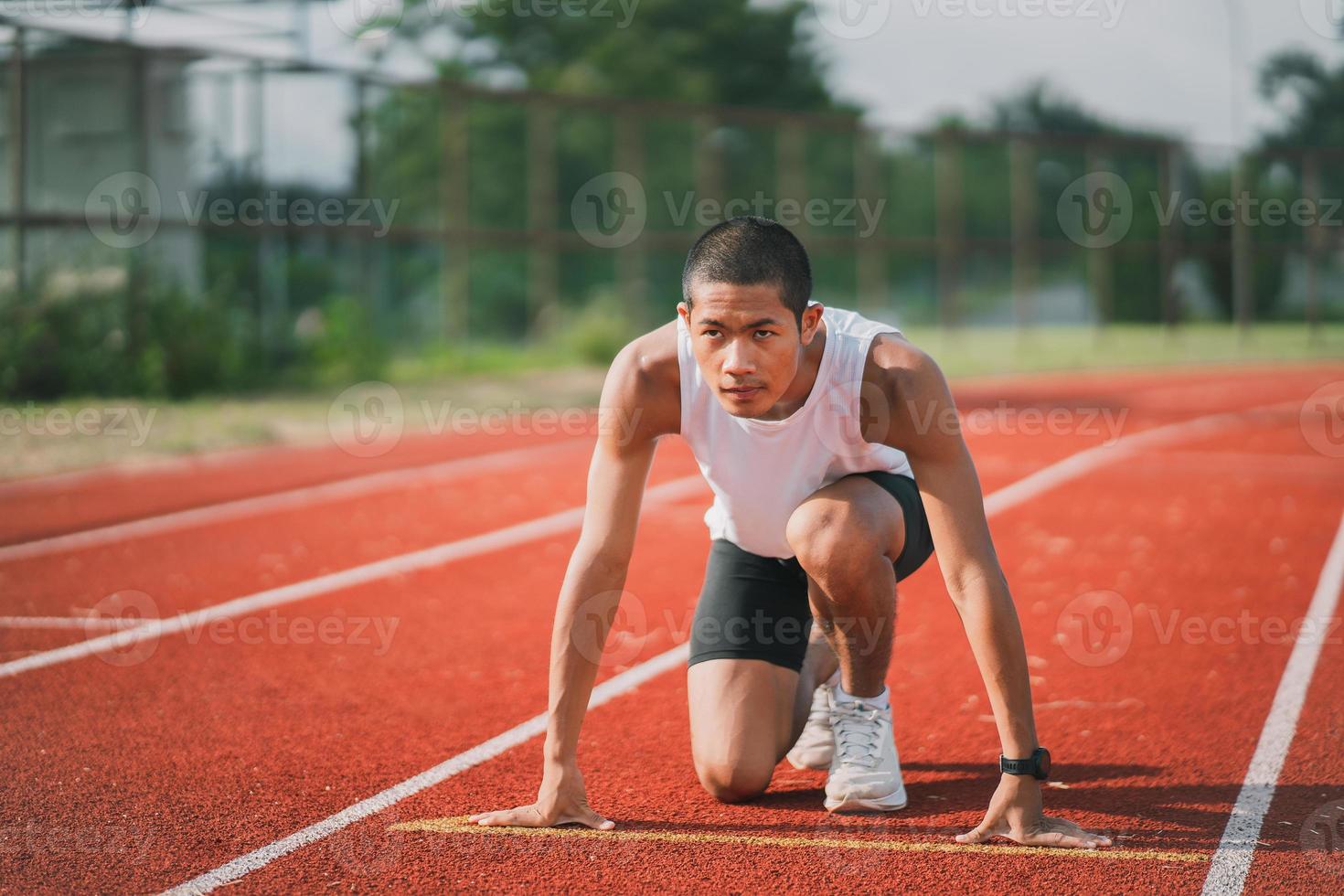 corredor de manos listo para comenzar a correr entrenamiento de atleta deportista correr en el carril en el estadio por la mañana. corredor hombre vestido con chaleco blanco para practicar correr prepararse para la carrera de competencia. foto