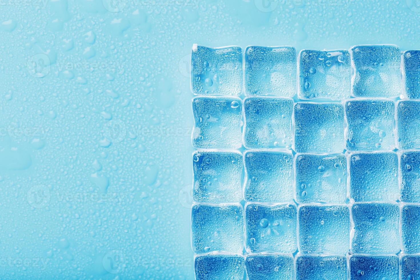 cubos de hielo con gotas de agua esparcidas sobre un fondo azul, vista superior. foto