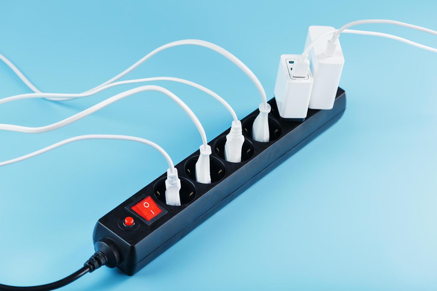A black mains filter with electrical outlets inserted into it with white plugs of electrical appliances on a blue background photo