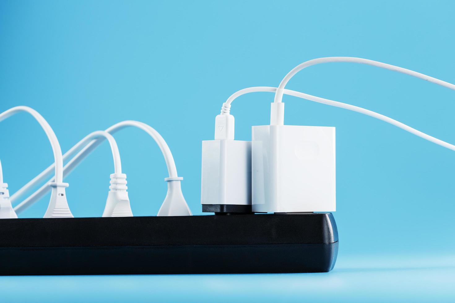 A black mains filter with electrical outlets inserted into it with white plugs of electrical appliances on a blue background photo