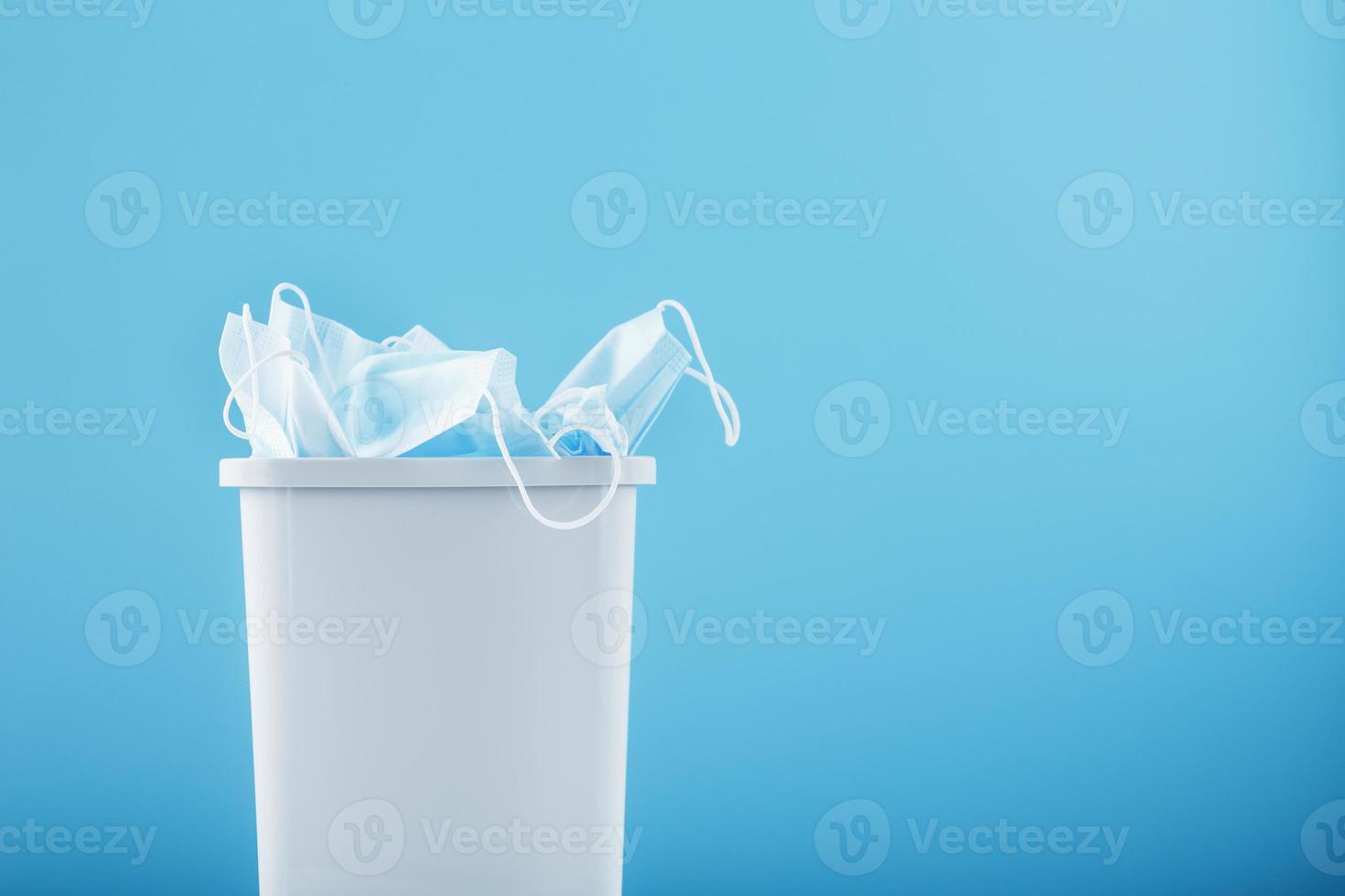 Waste bin full of used protective masks on a light blue background with free space. photo