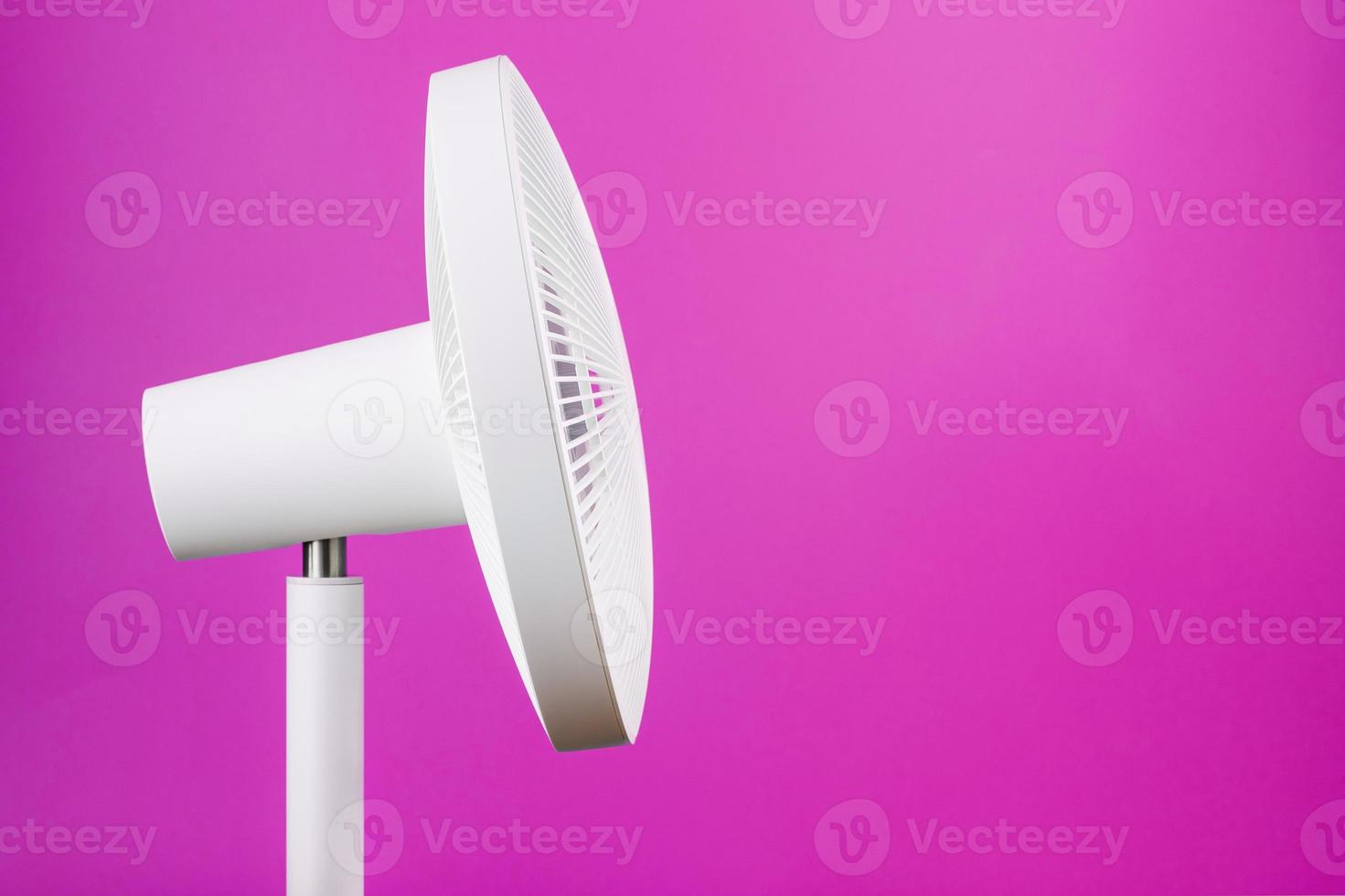 White modern electric fan for cooling the room on a pink background. photo