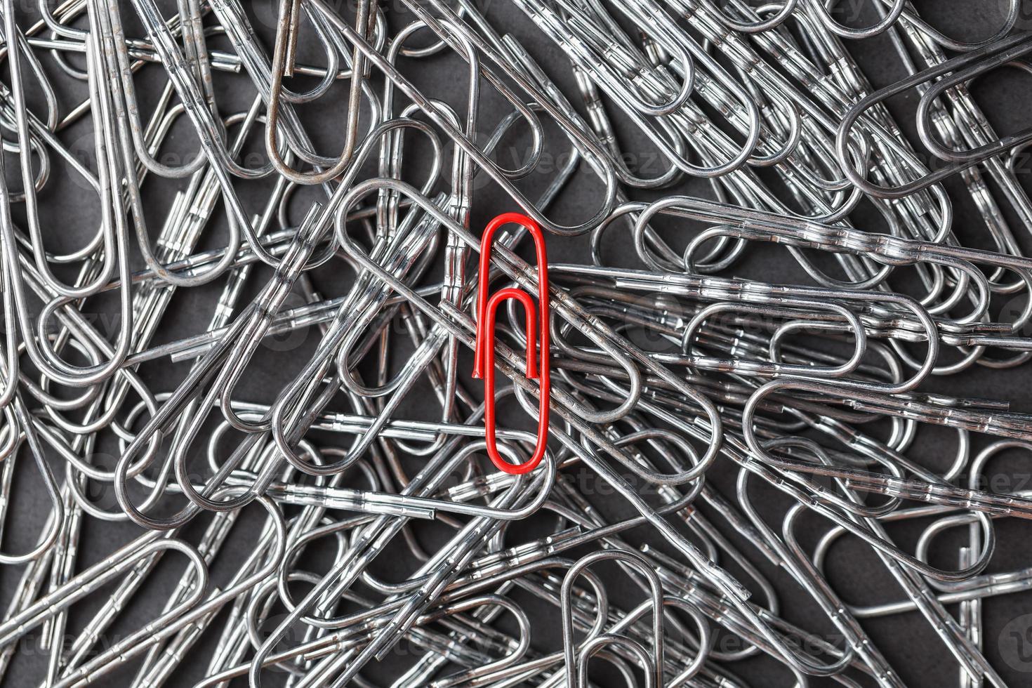 A red paper clip stands out against a textured background of silver paper clips photo