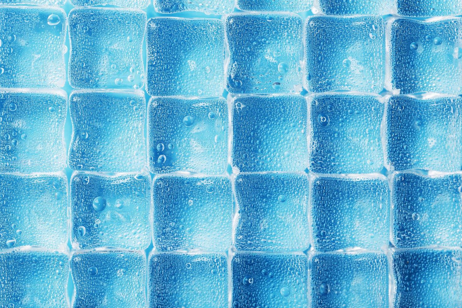 muchos cubitos de hielo helados y refrescantes con gotas sobre un fondo azul foto