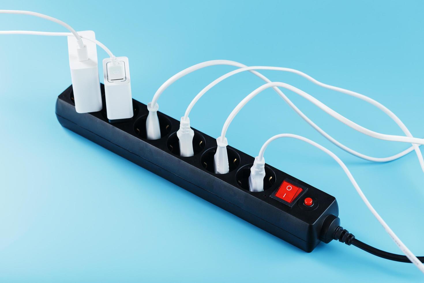 Black surge protector with a red button and connected white wires of electrical appliances on a blue background. photo