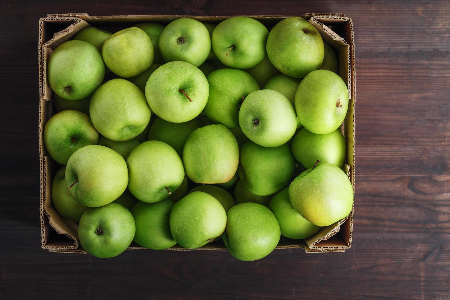 manzanas verdes en una caja sobre una mesa de madera, vista superior. foto