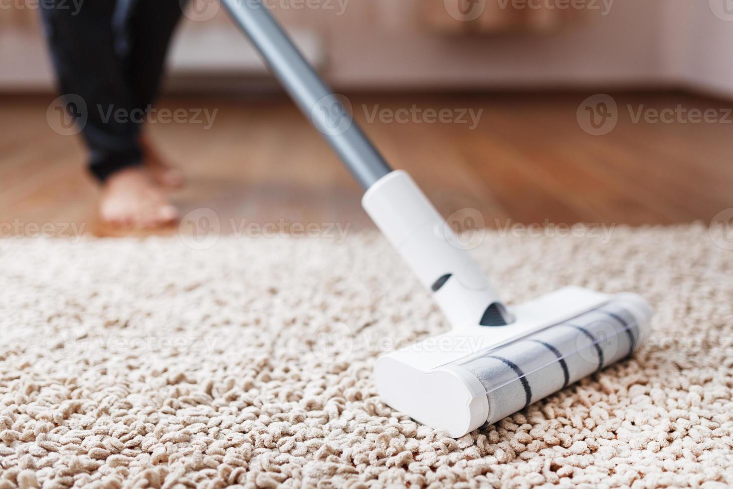 Human legs and a white turbo brush of a cordless vacuum cleaner cleans the carpet in the house photo