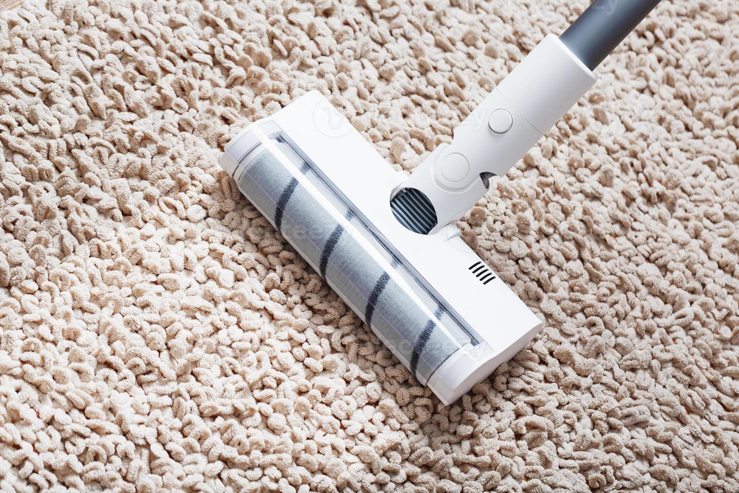 A cordless vacuum cleaner cleans the carpet in the living room with the bottom of the legs With a clean stripe photo