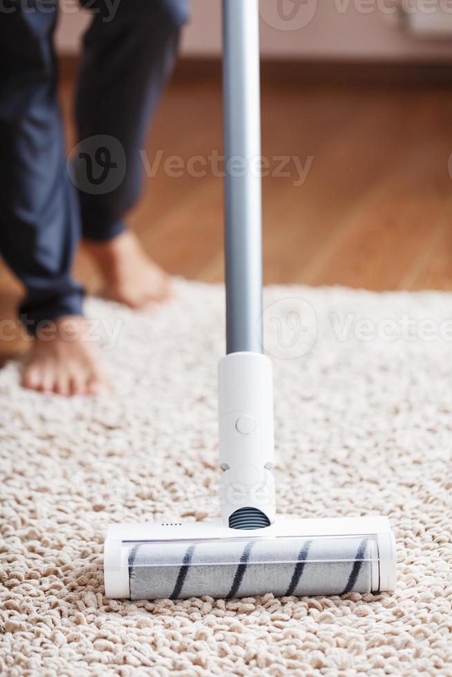 Human legs and a white turbo brush of a cordless vacuum cleaner cleans the carpet in the house photo