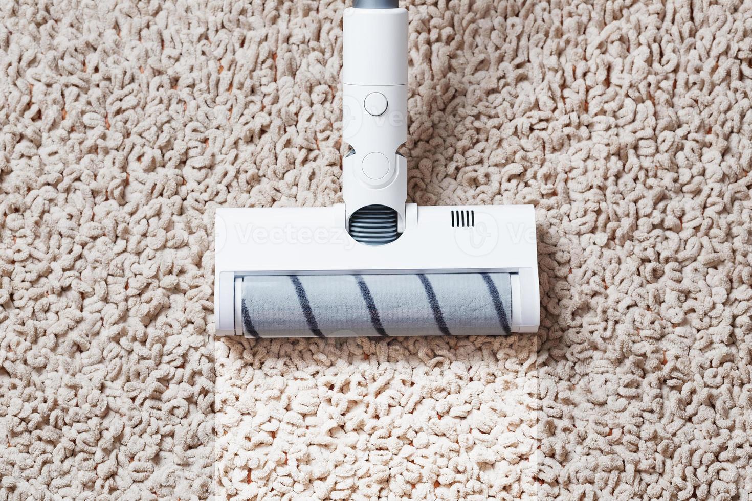 A cordless vacuum cleaner cleans the carpet in the living room with the bottom of the legs With a clean stripe photo