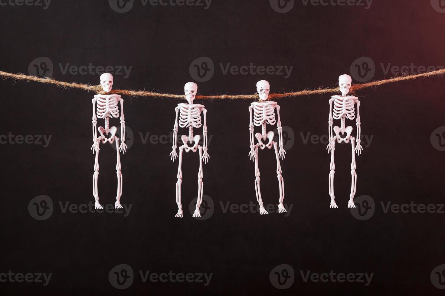 Skeletons hang on a rope on a black background with red illumination photo