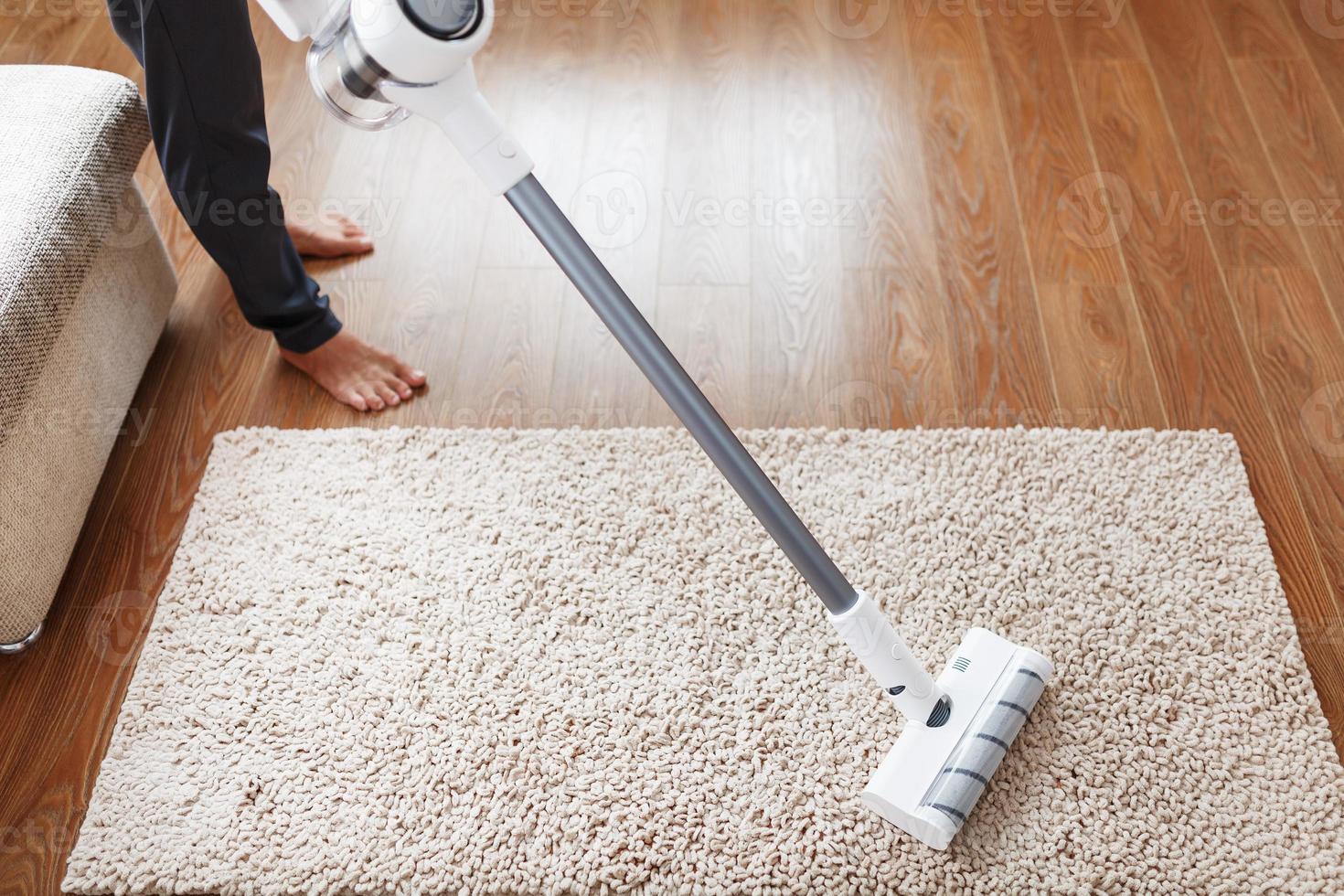 una aspiradora inalámbrica limpia la alfombra de la sala de estar con la  parte inferior de las piernas. 11070993 Foto de stock en Vecteezy