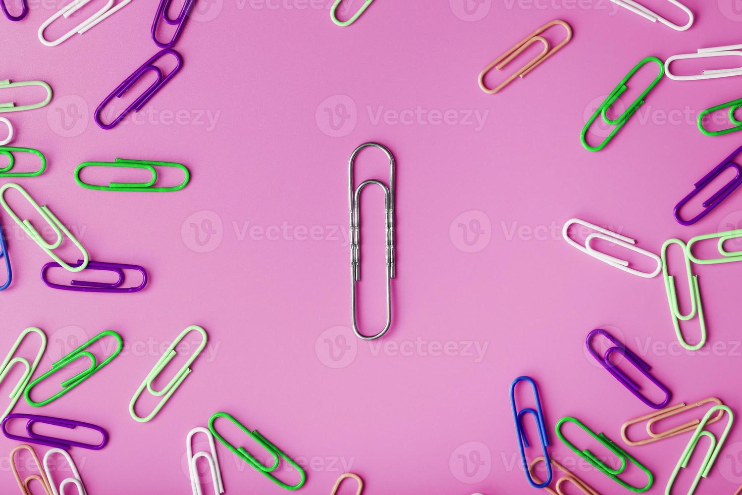 A large paper clip surrounded by small colored paper clips on a pink background photo