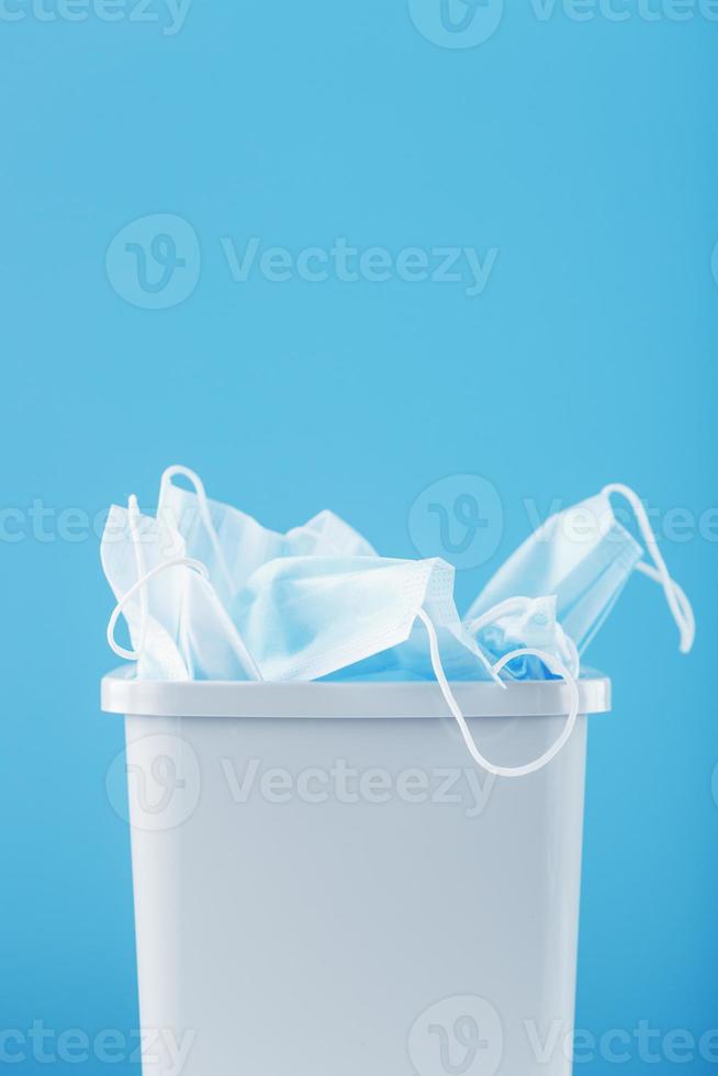 Waste bin full of used protective masks on a light blue background with free space. photo