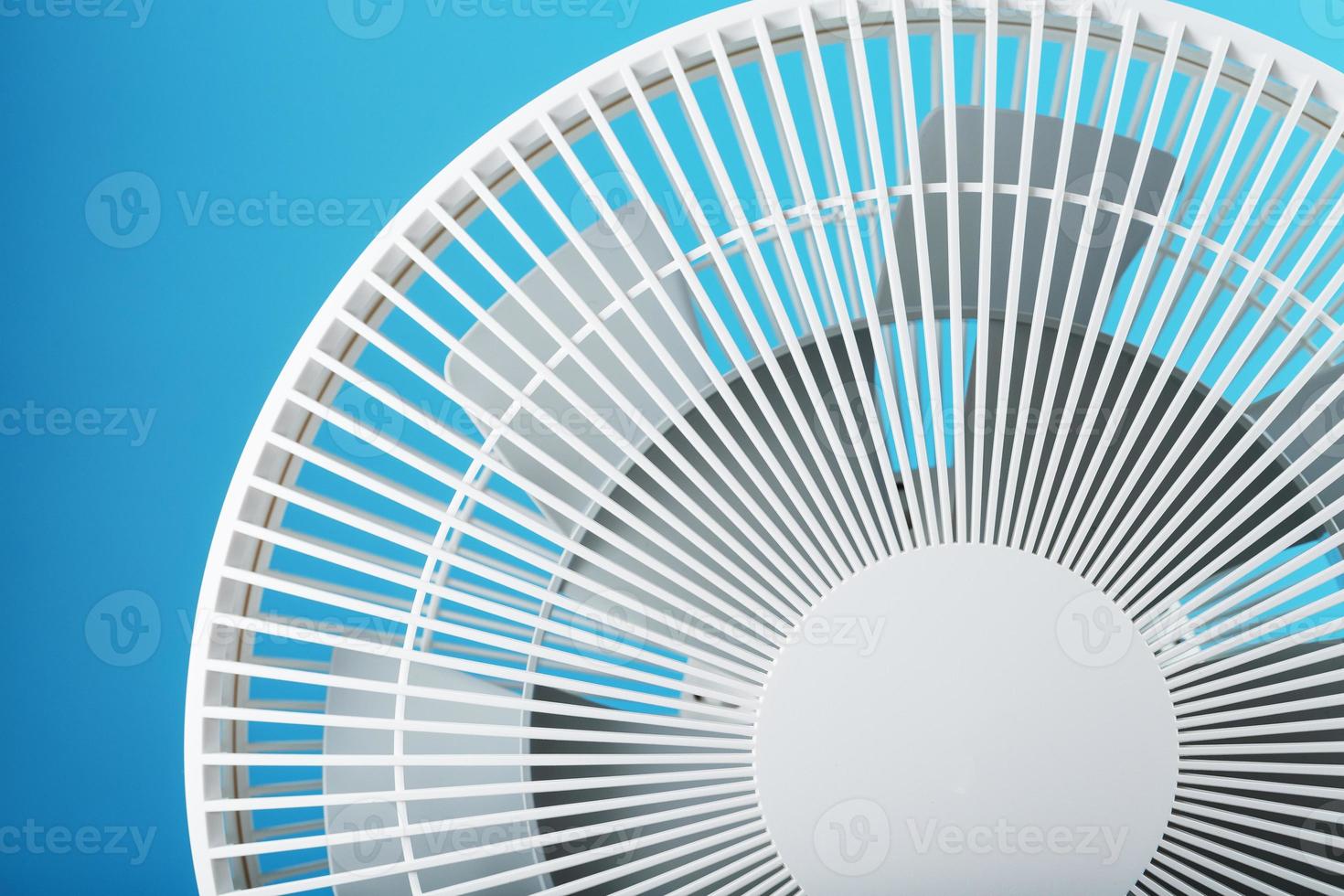 The grille and blades of the electric fan are white on a blue background photo