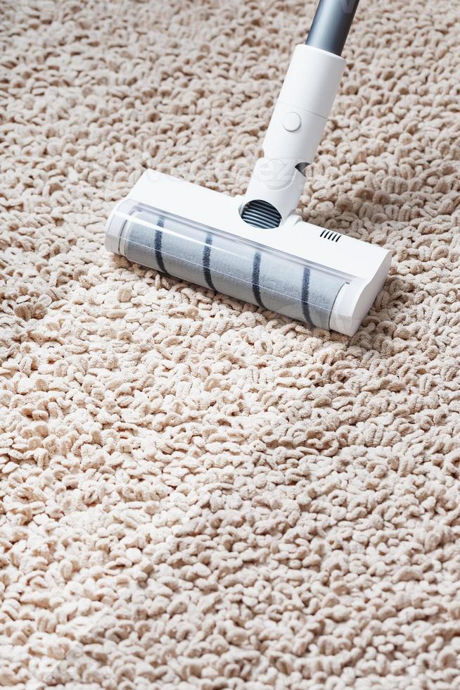 A cordless vacuum cleaner cleans the carpet in the living room with the bottom of the legs With a clean stripe photo