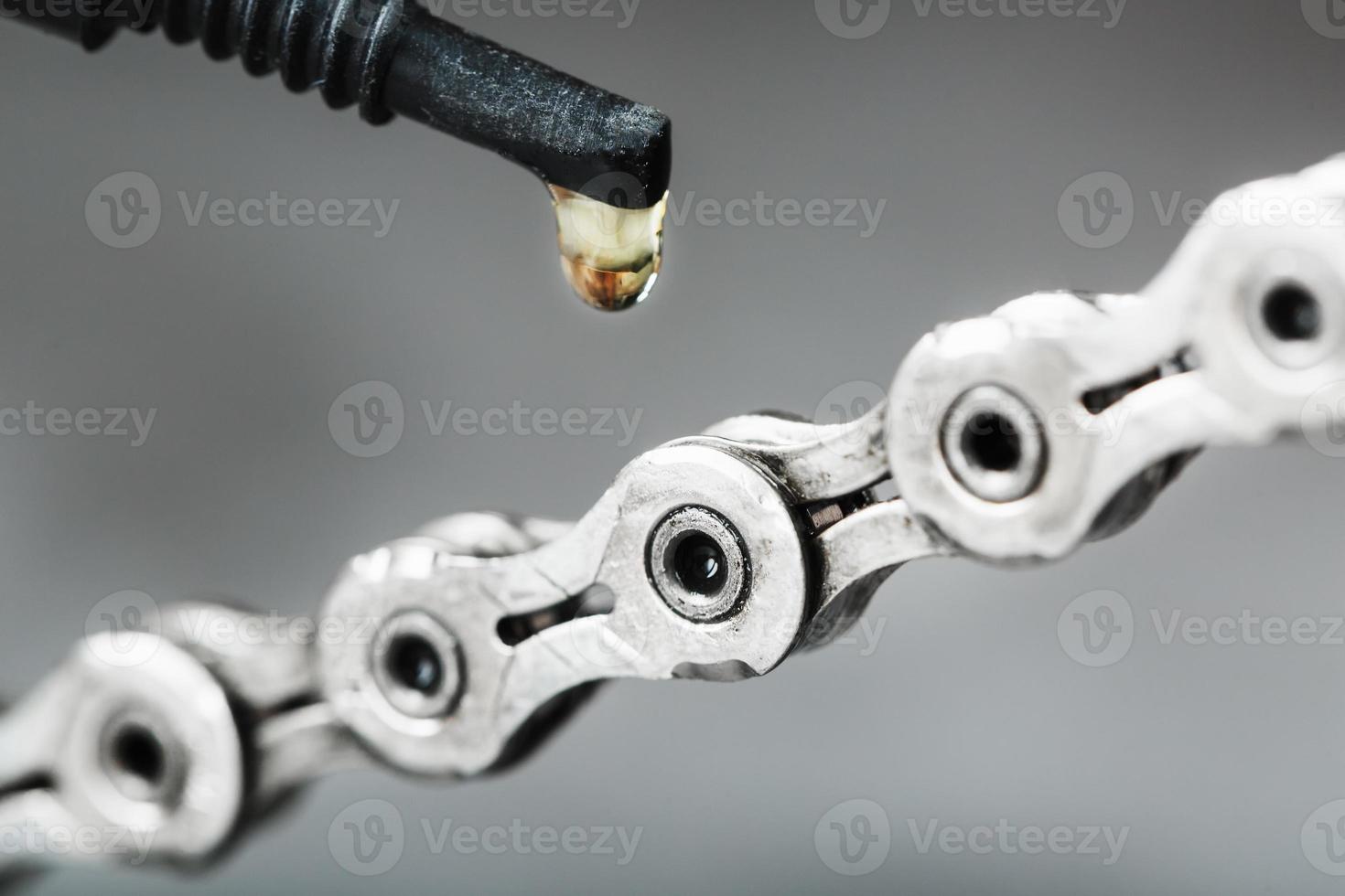 engrasando una cadena de bicicleta con una gota de aceite dorado en un fondo gris foto