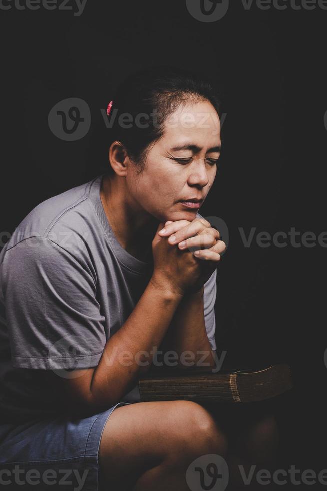 la mano de una mujer cristiana en la sagrada biblia es orar y adorar gracias a dios en la iglesia con antecedentes negros, concepto de fe, espiritualidad y religión foto