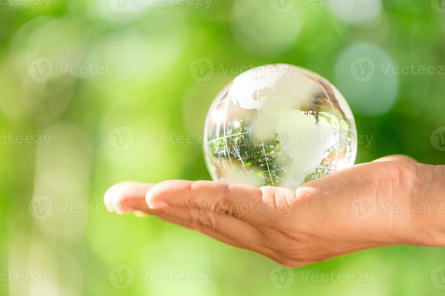 Human hand holding globe planet glass In green forest with bokeh nature lights. world environment day. concept for environment conservation, protect ecology earth and environmental eco-friendly life. photo