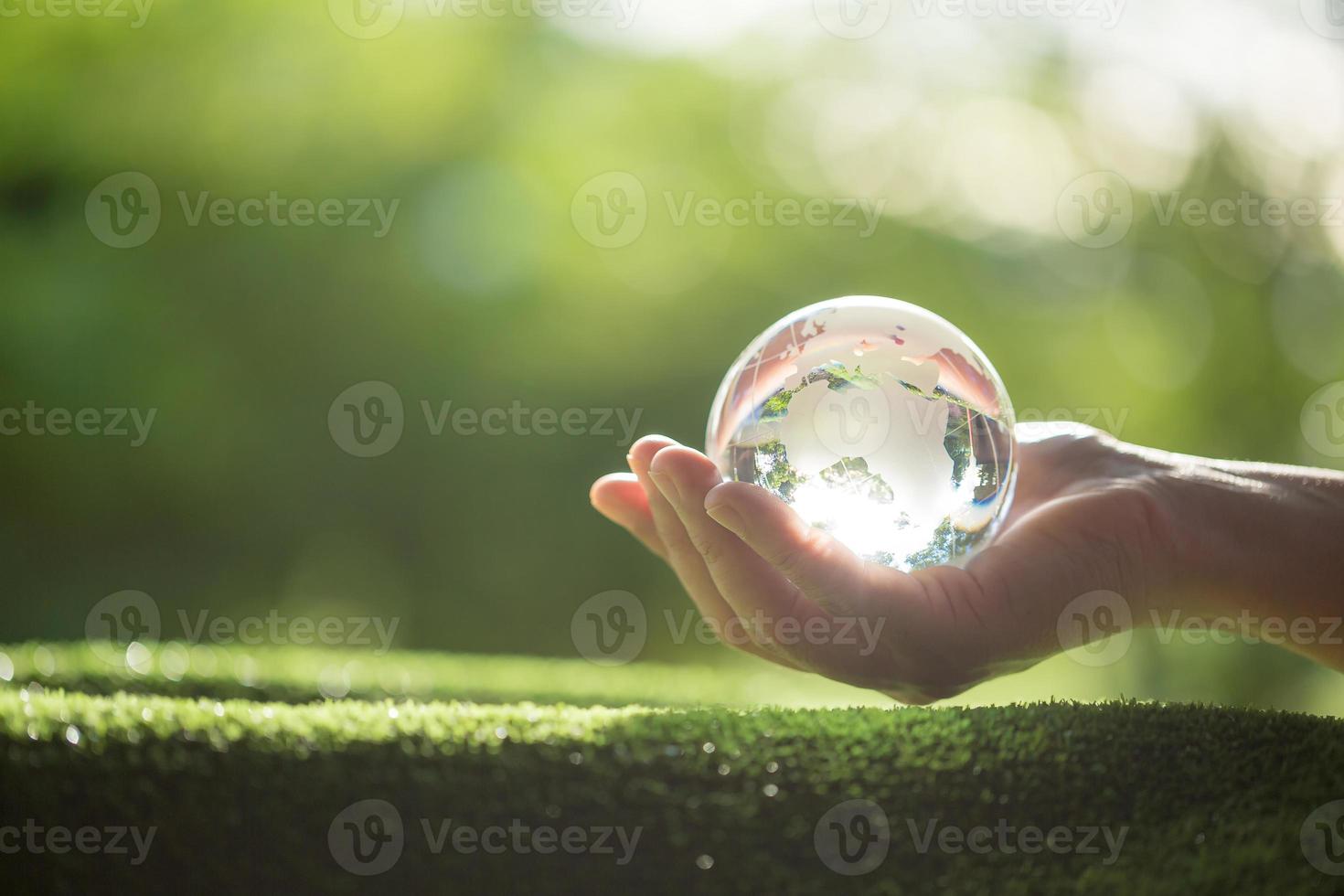 mano humana sosteniendo globo planeta cristal en bosque verde con luces de naturaleza bokeh. día Mundial del Medio Ambiente. concepto para la conservación del medio ambiente, proteger la ecología de la tierra y la vida ecológica. foto