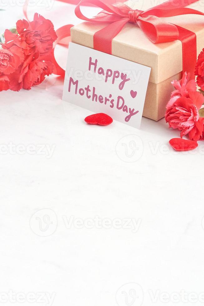 Mother's Day gift background, red carnation flower bouquet with wrapped kraft gift tied with ribbon isolated on marble white background, close up. photo