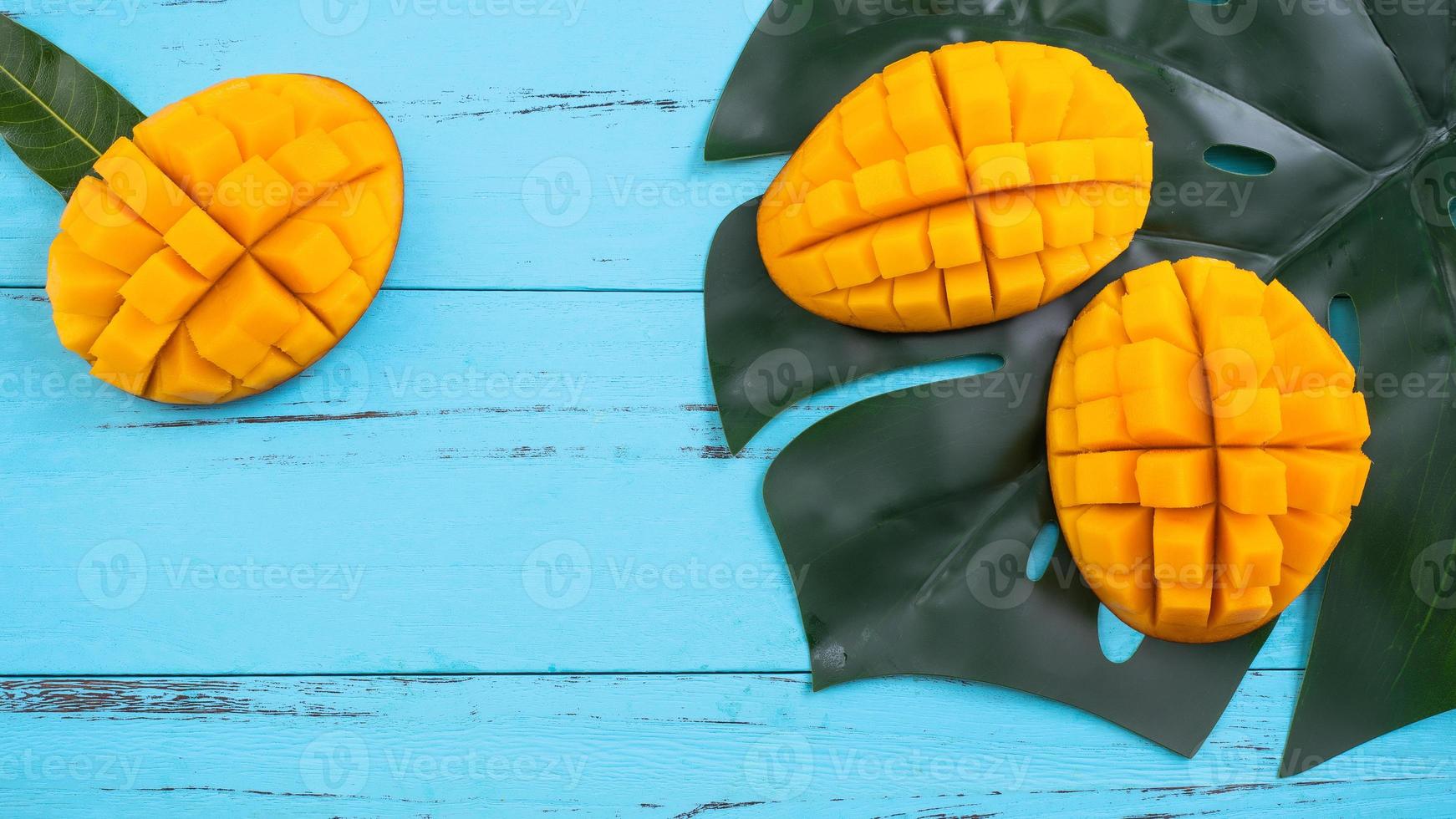 Mango - Fresh chopped tropical mango fruit isolated on bright vibrant light blue wooden table background, top view, flat lay layout, overhead shot. photo