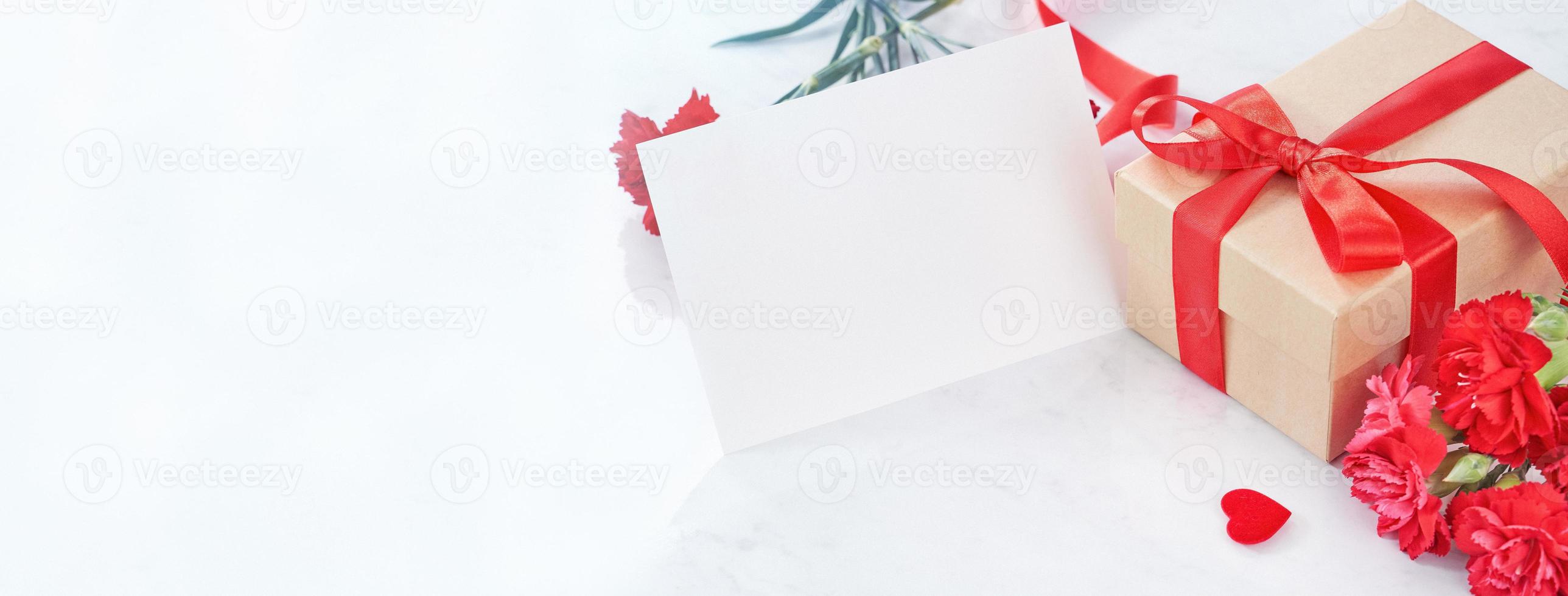 Mother's Day gift background, red carnation flower bouquet with wrapped kraft gift tied with ribbon isolated on marble white background, close up. photo