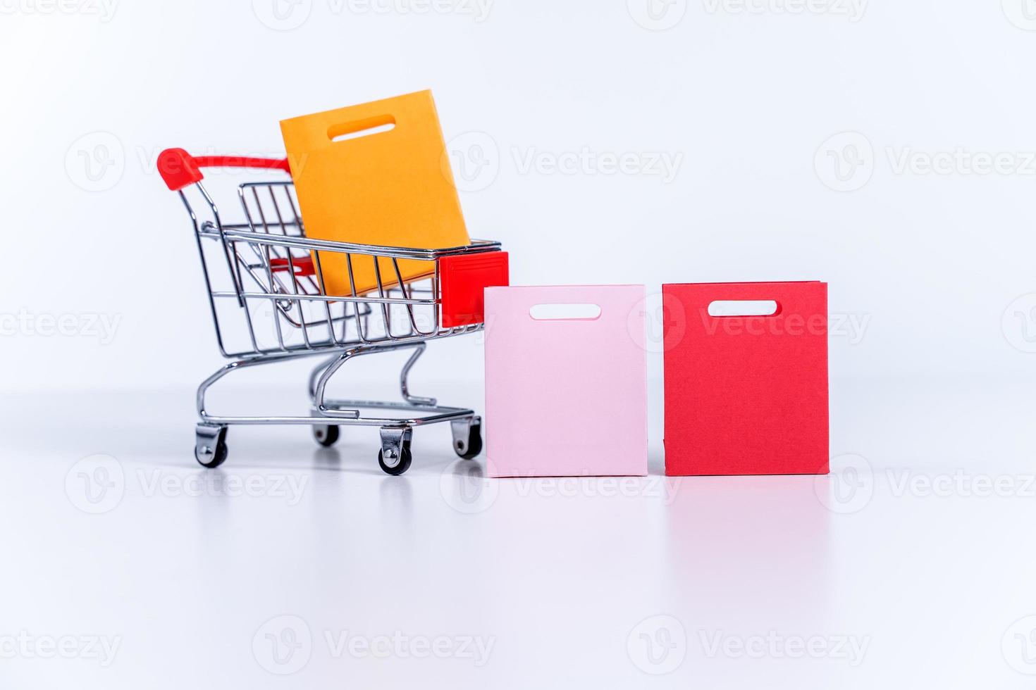 Shopping bags in a silver red shopping cart isolated on white table background, concept of staying home order, close up, copy space design. photo