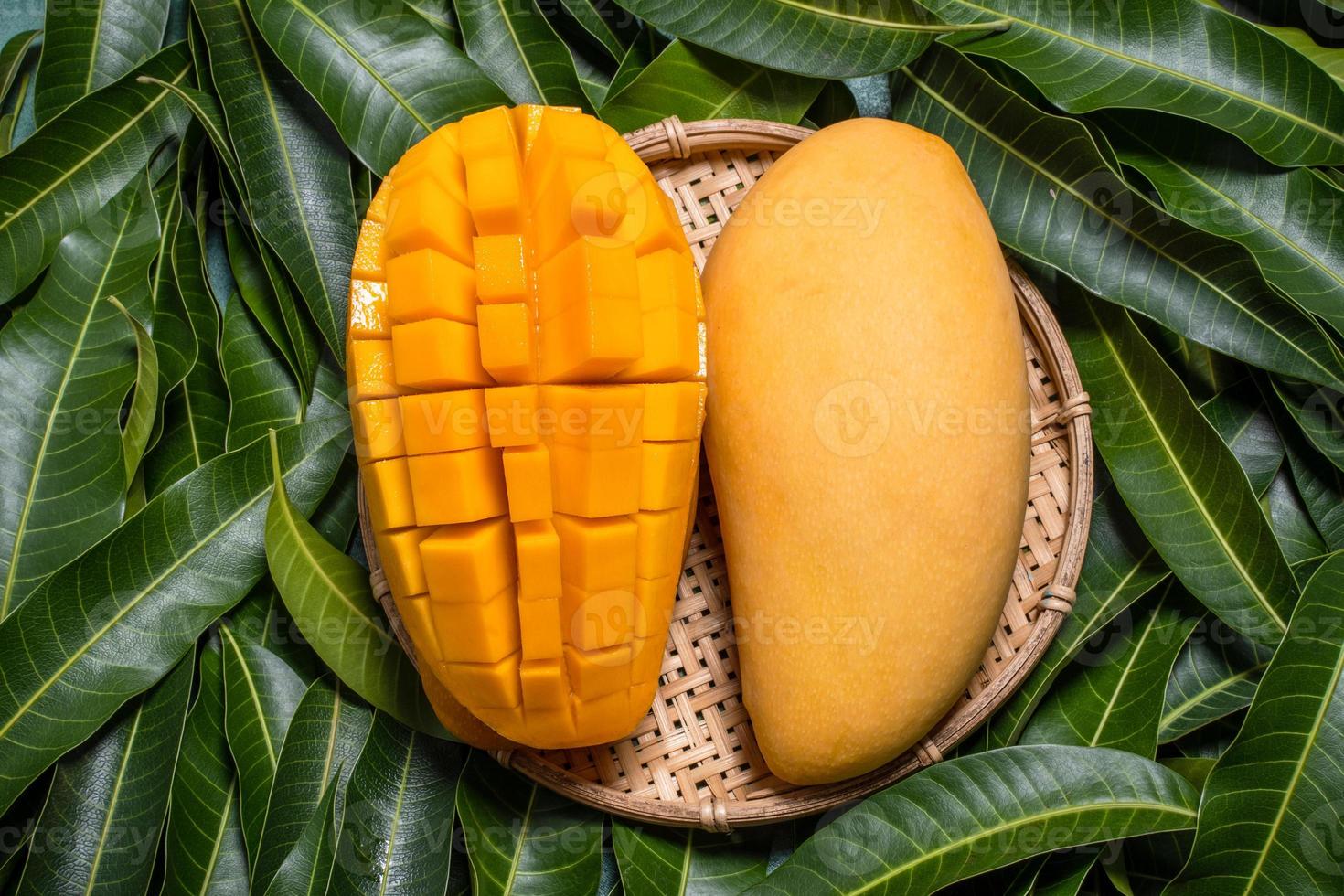 mango, fruta tropical, en una cesta tamiz de madera de bambú sobre fondo de hoja verde, vista superior, marco completo, hermoso concepto de diseño de cosecha madura. foto