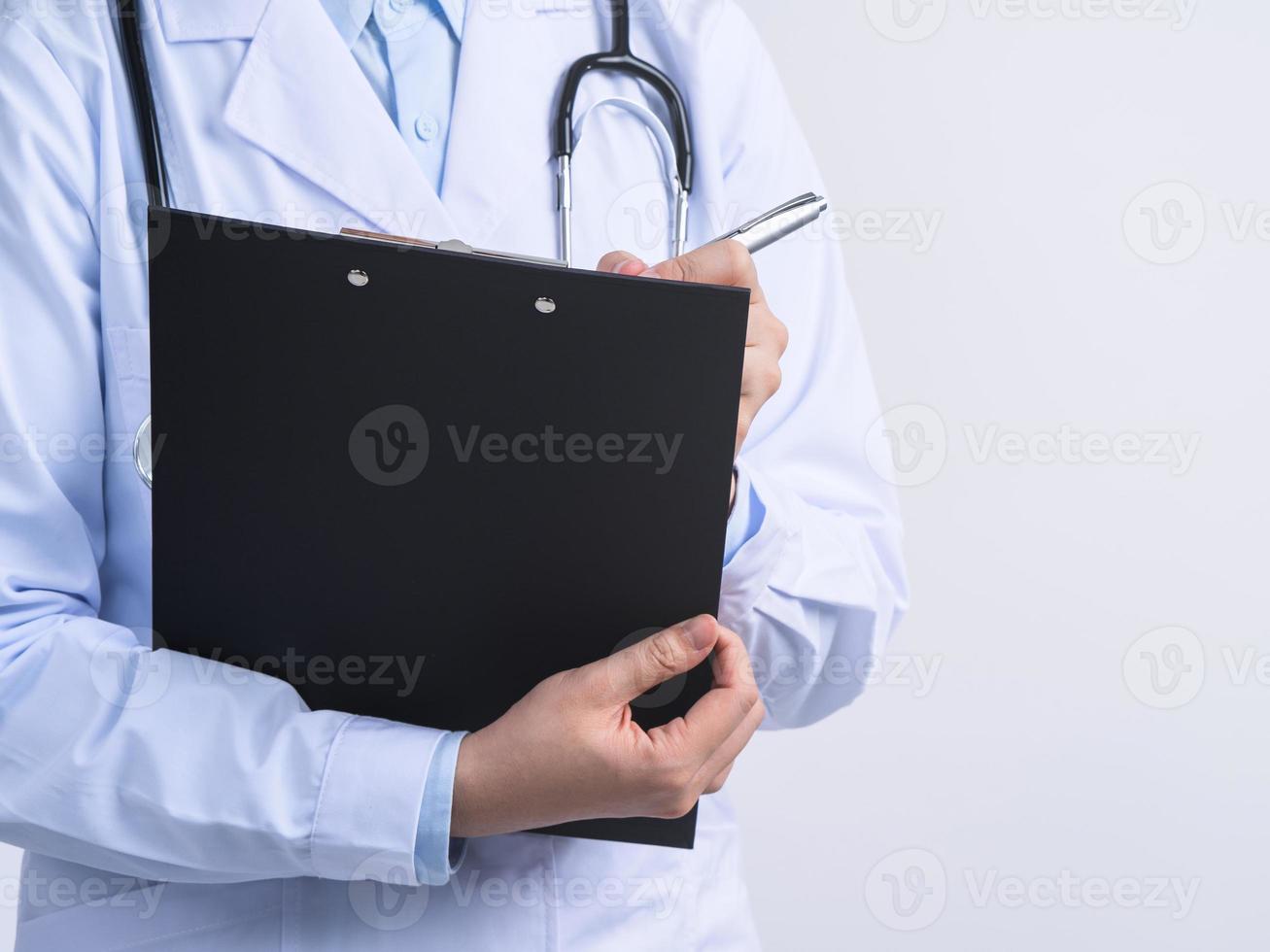 Doctor with stethoscope in white coat holding clipboard, writing medical record diagnosis, isolated on white background, close up, cropped view. photo