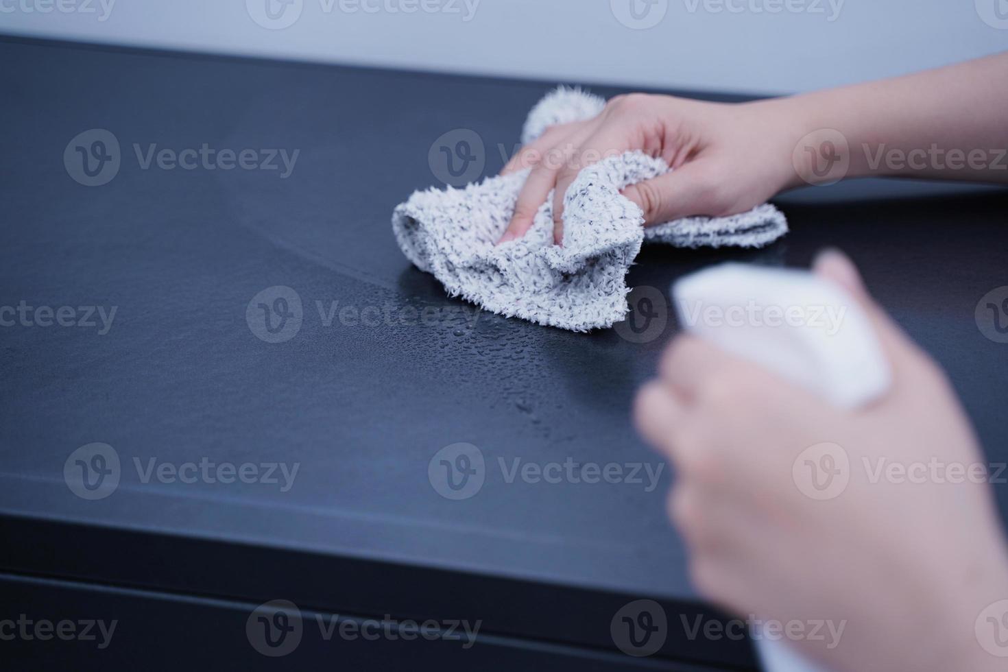 la mujer joven está sosteniendo una botella de spray, un trapo para limpiar, limpiar la superficie de alojamiento del estante del gabinete de metal de la oficina, cerrar, estilo de vida, concepto de antibacteriano. foto