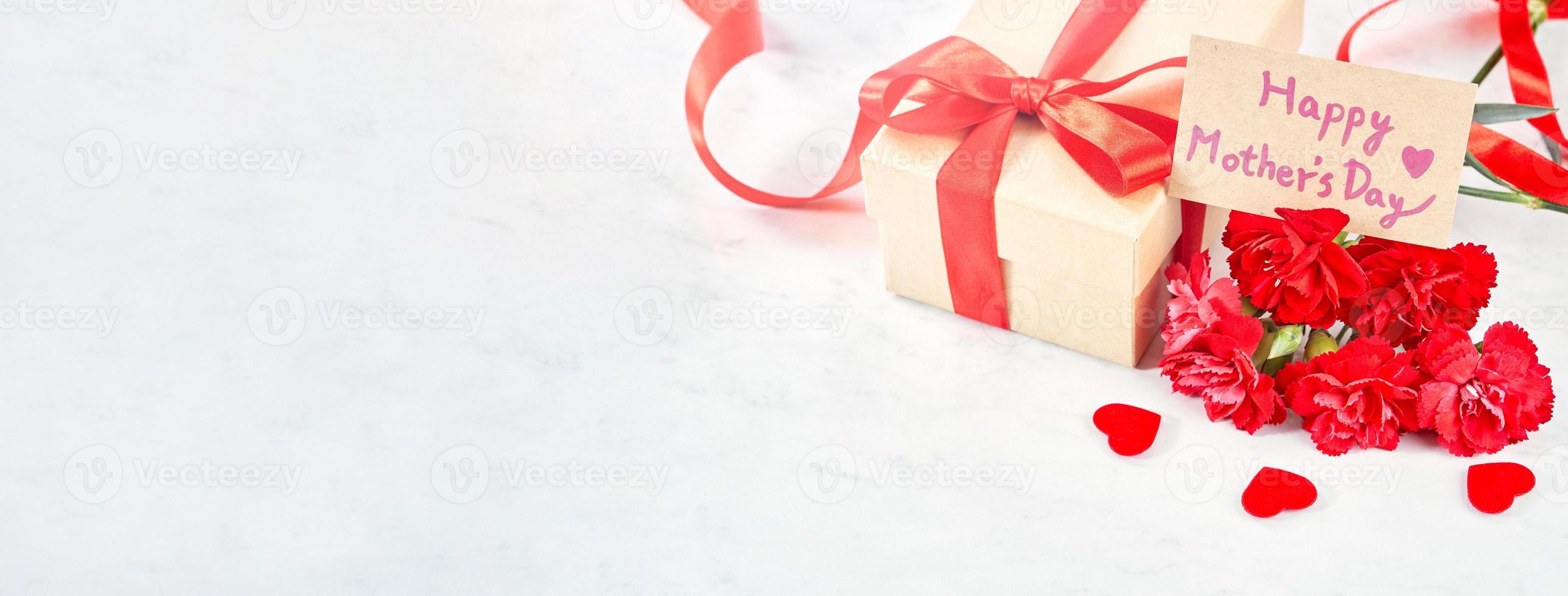 Mother's Day gift background, red carnation flower bouquet with wrapped kraft gift tied with ribbon isolated on marble white background, close up. photo