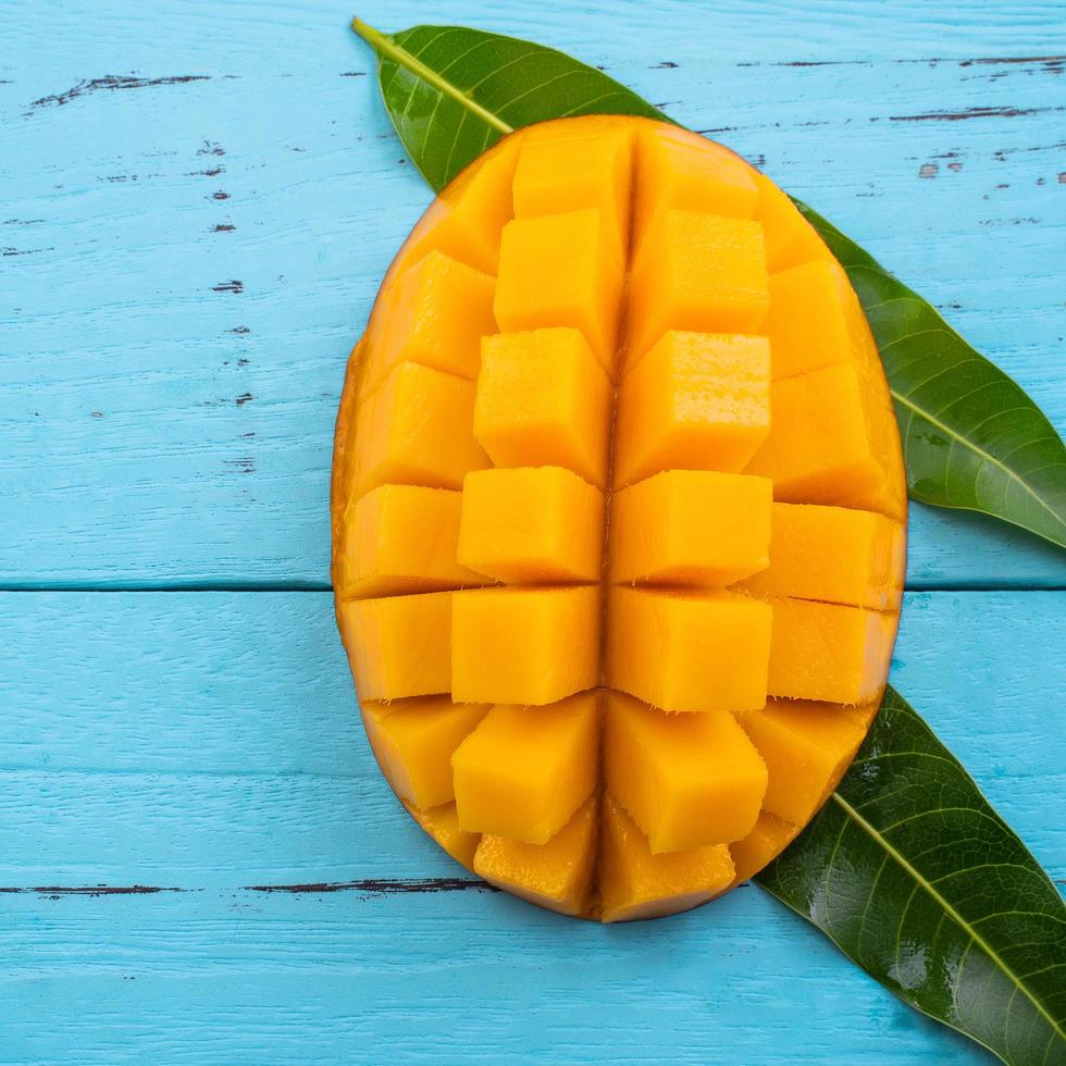 Mango - Fresh chopped tropical mango fruit isolated on bright vibrant light blue wooden table background, top view, flat lay layout, overhead shot. photo