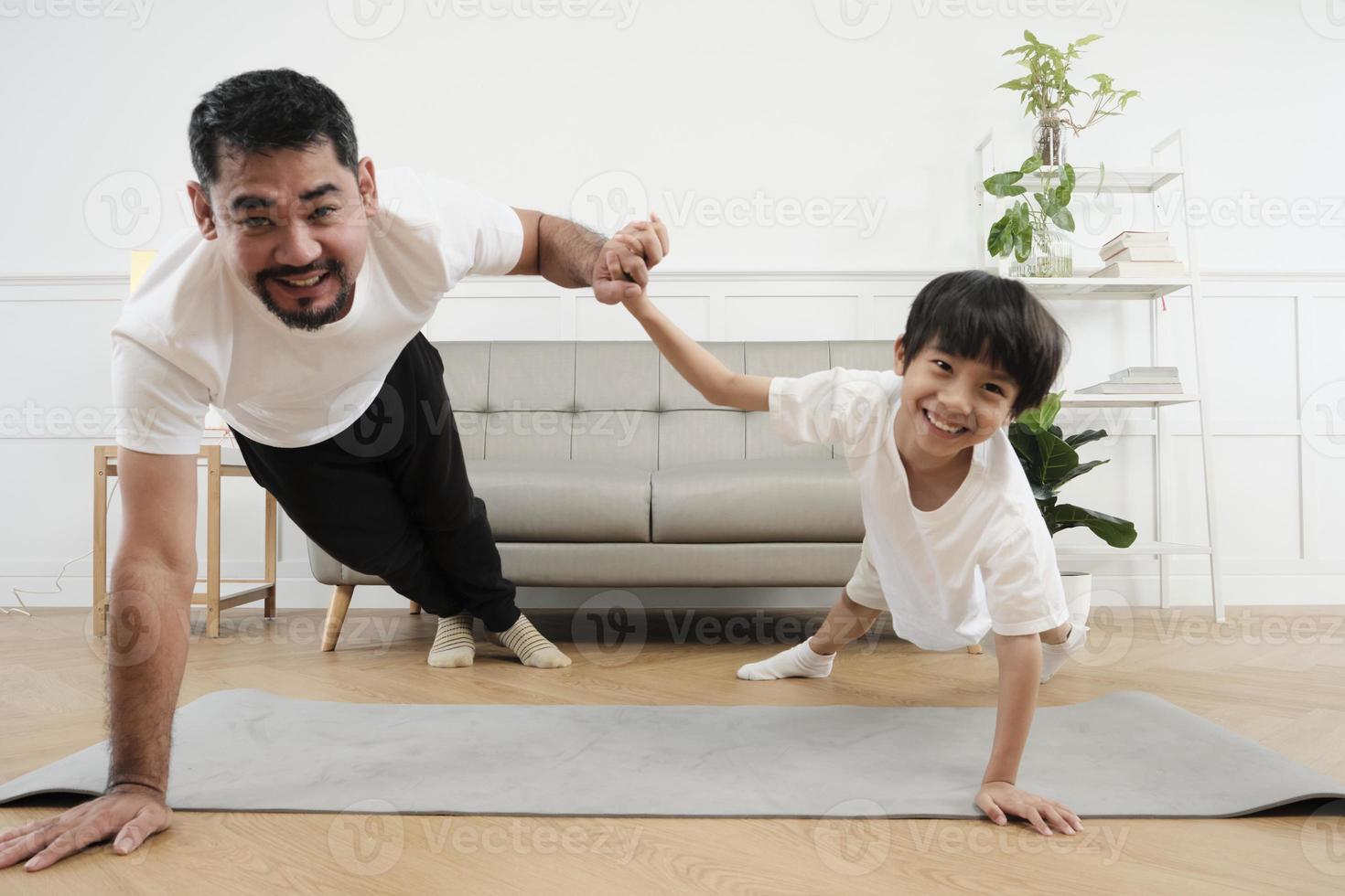 Young Asian Thai father lovely trains her little son to exercise and practices yoga on living room floor together for healthy fitness and wellness, happy domestic home lifestyle on family weekends. photo