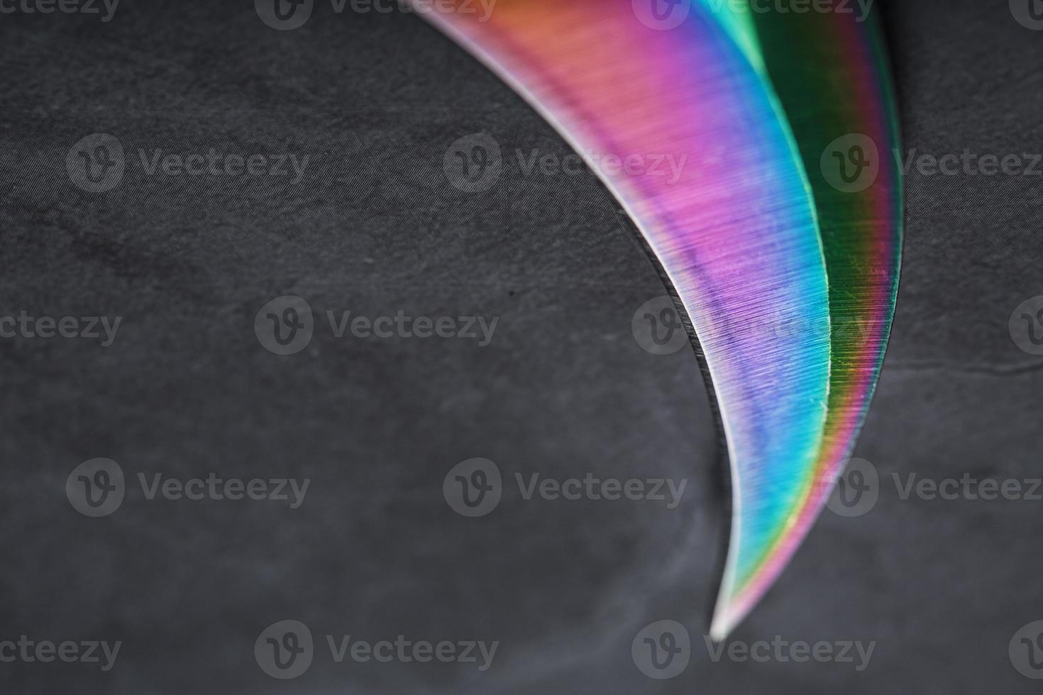 la hoja curva afilada de la daga kerambit es un color arcoiris degradado sobre un fondo oscuro. foto