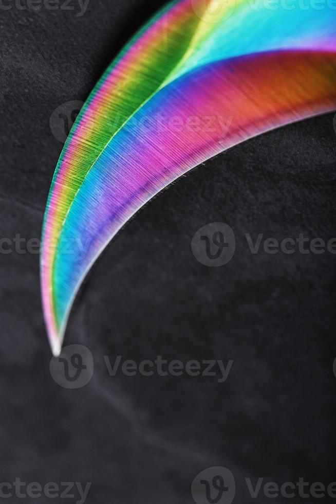 The sharp blade of the Kerambit knife made of steel is multicolored in close-up on a dark background. photo