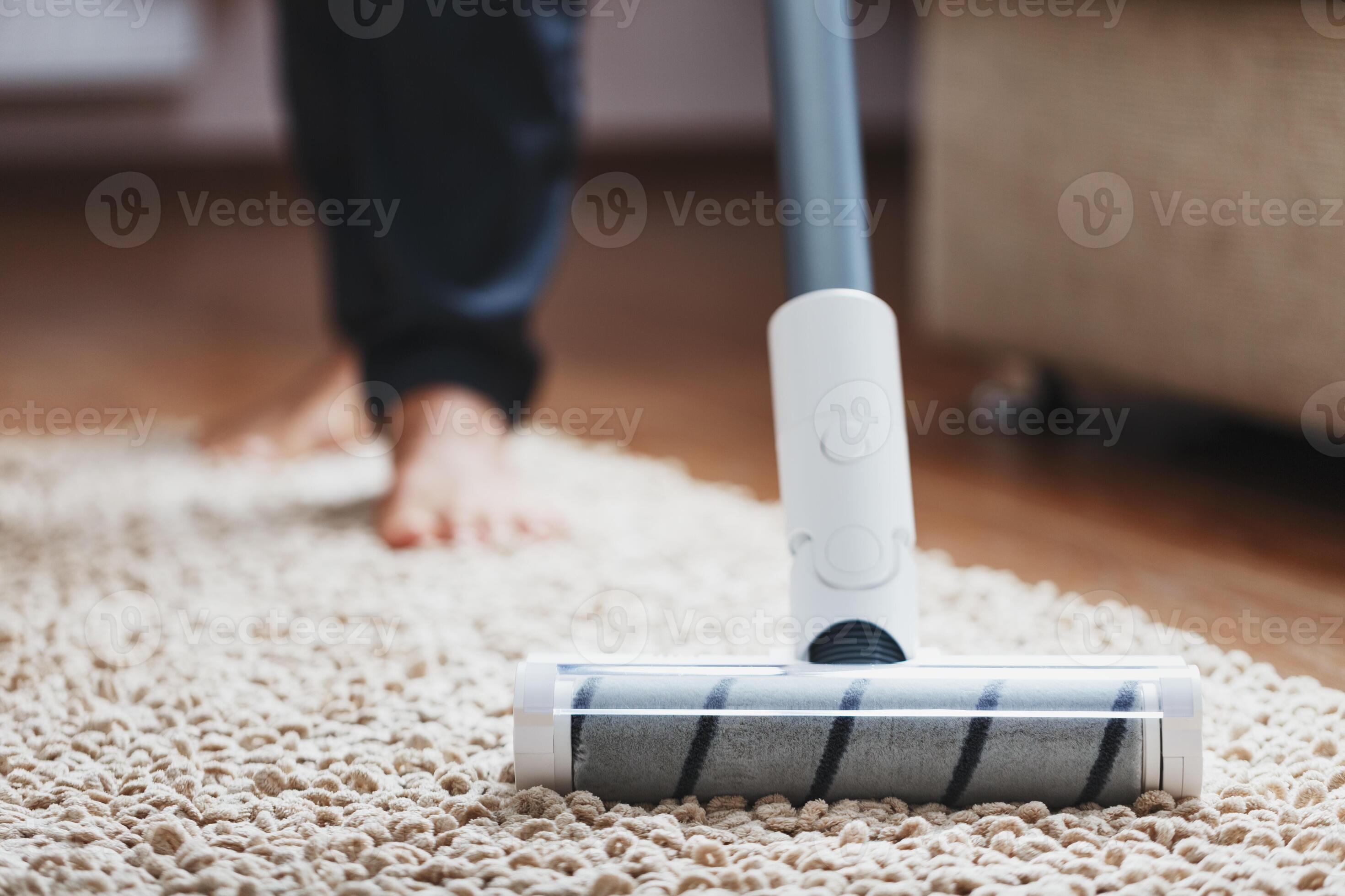 Human legs and a white turbo brush of a cordless vacuum cleaner cleans