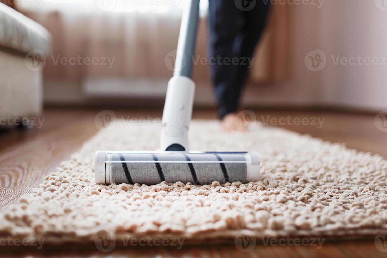 Human legs and a white turbo brush of a cordless vacuum cleaner cleans the carpet in the house photo