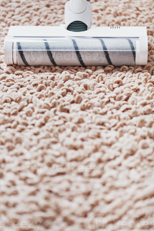 The turbo brush of a cordless vacuum cleaner cleans the carpet in the house in close-up photo