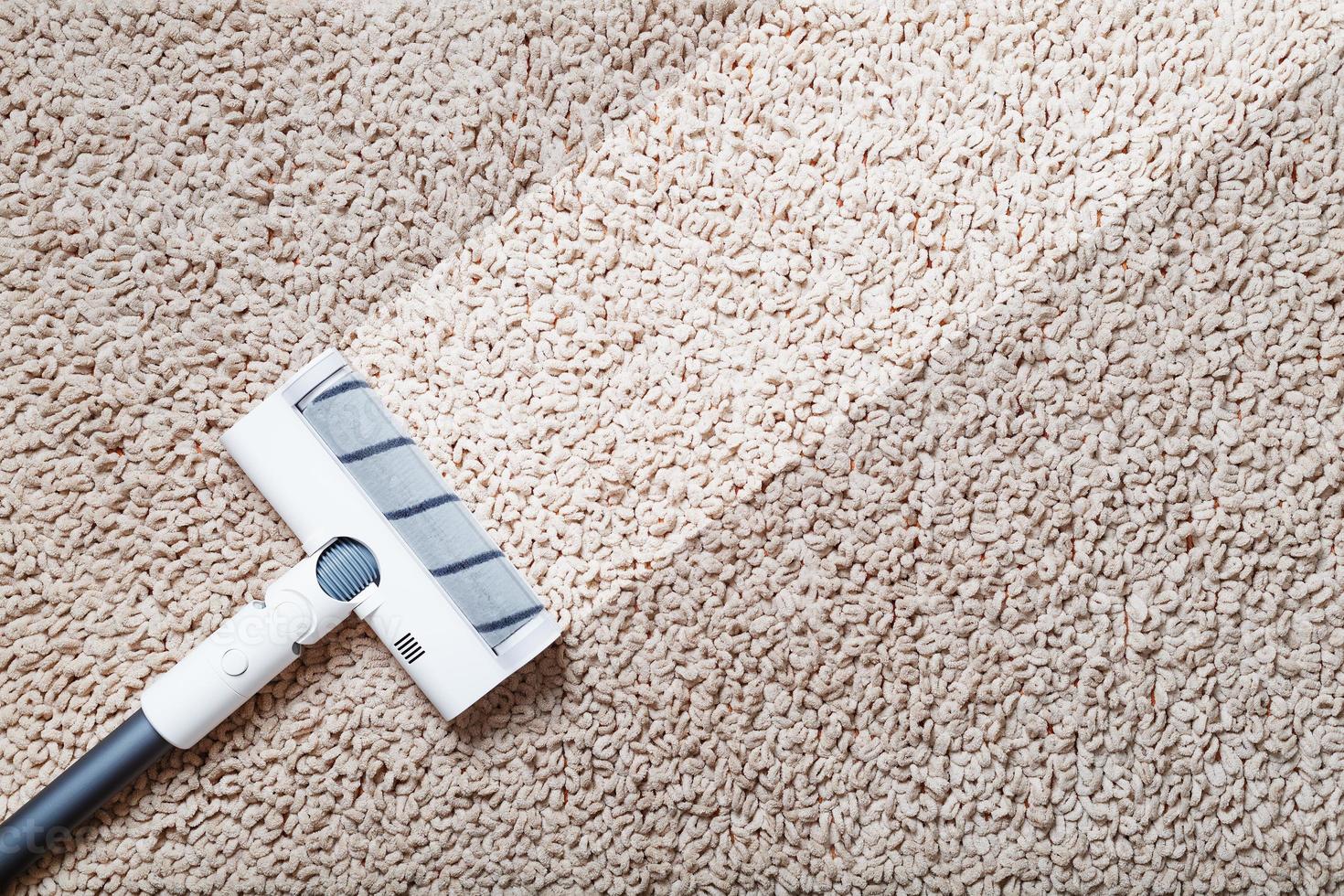 una aspiradora inalámbrica limpia la alfombra en la sala de estar con la parte inferior de las piernas con una raya limpia foto